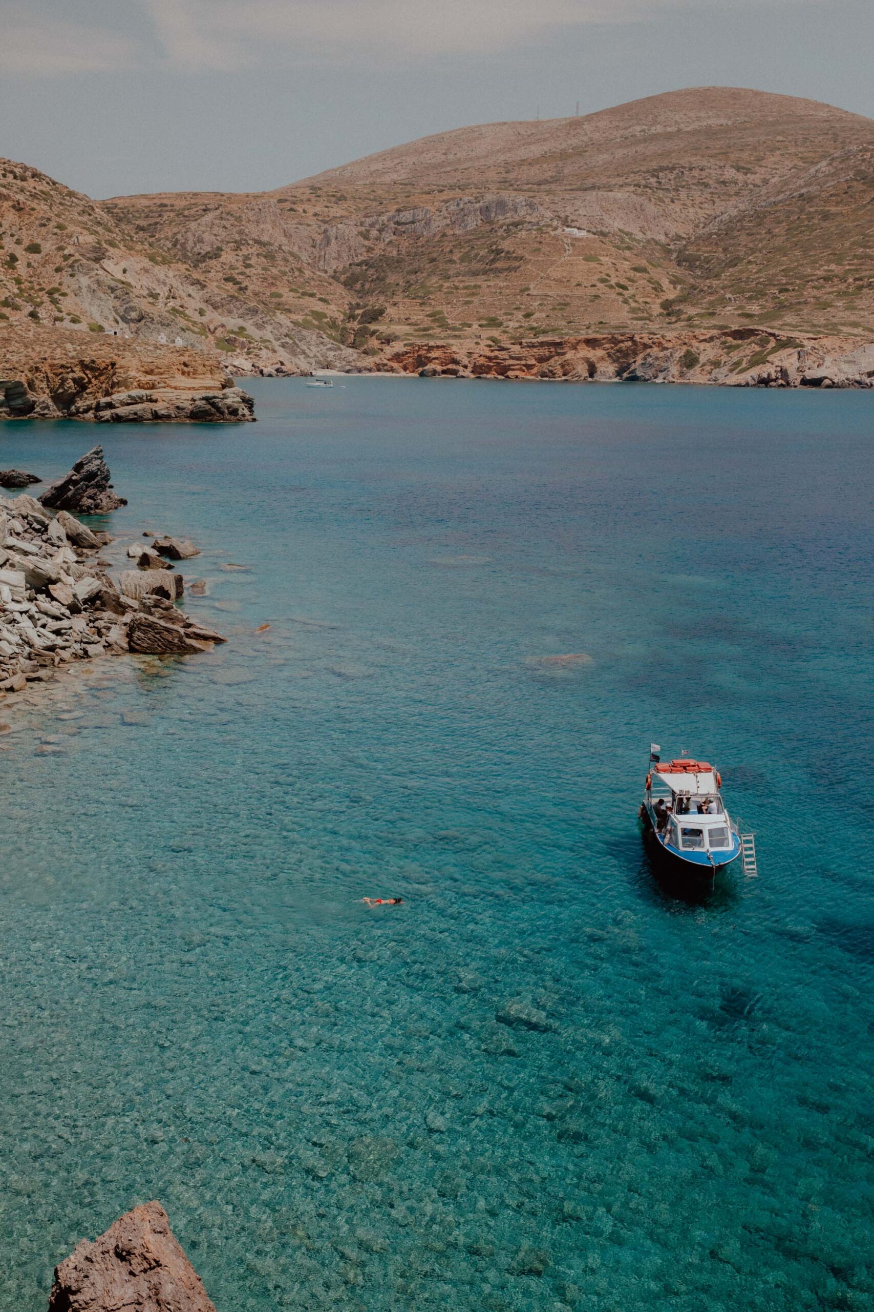Boat and swimmer in turquoise waters of Agali Beach Folegandros with dramatic cliff backdrop and crystal clear sea