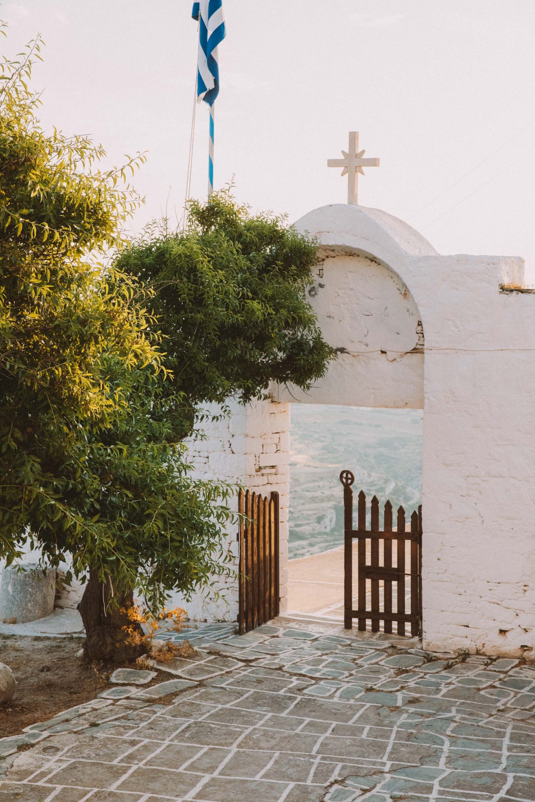 Golden sunset view from inside Church of Panagia Folegandros framed by traditional white archway and greek flag