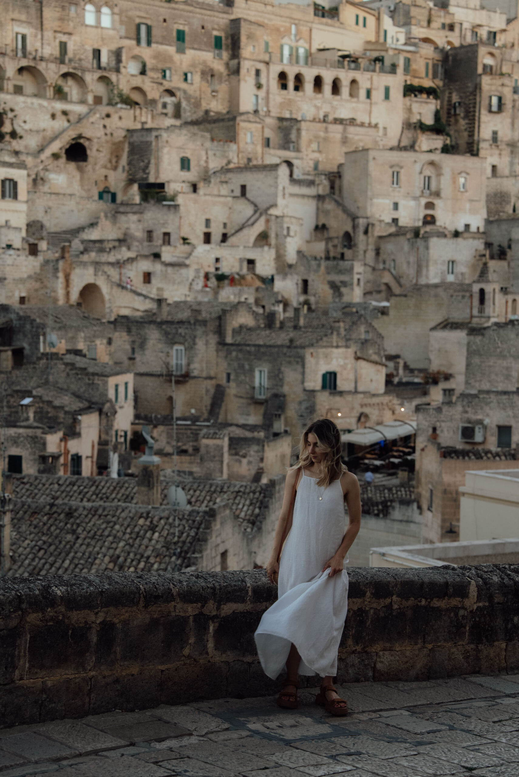 Best sunset view of Matera Italy with person showing layered cave dwellings carved into limestone cliffs