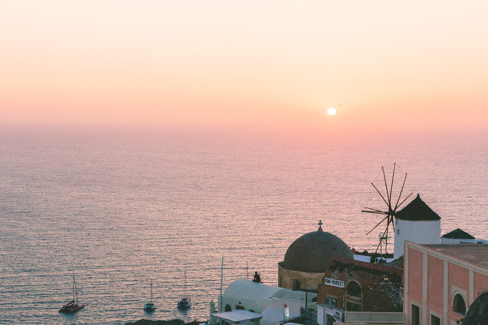 A serene Santorini sunset with a silhouette of a windmill, overlooking the Aegean Sea and pastel-hued skies