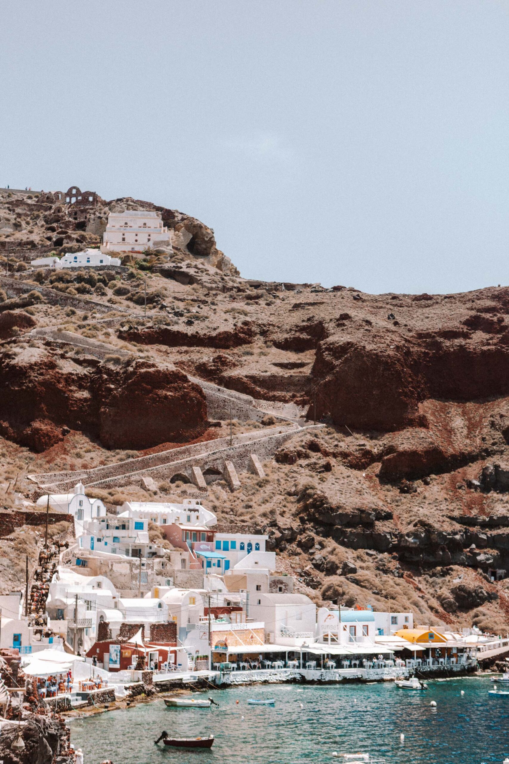 Ammoudi Bay in Santorini, Greece, featuring colorful buildings, rocky cliffs, and boats docked by the crystal-clear waters.