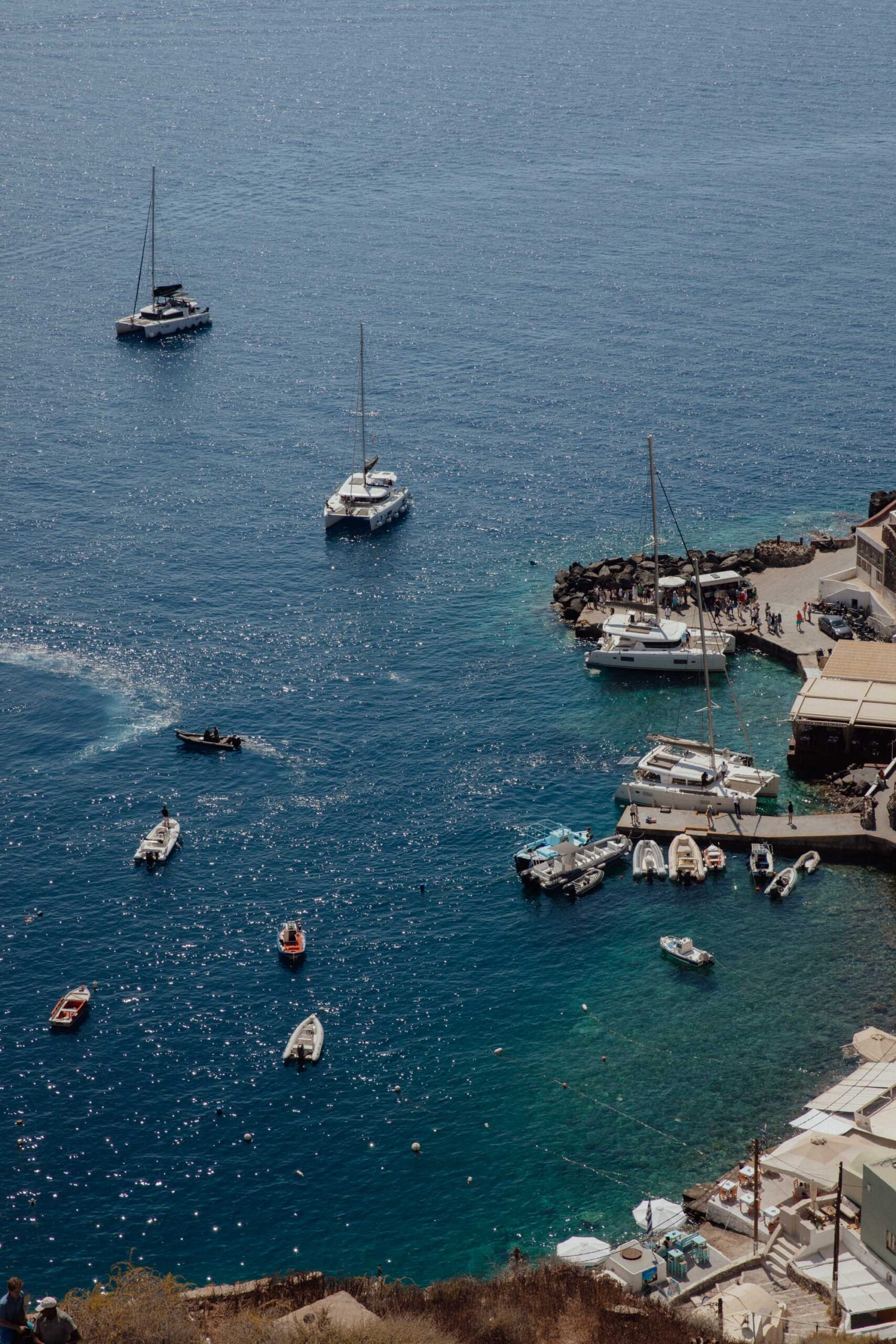 View of Santorini’s harbor with turquoise waters, docked boats, and a cliffside village in the background.