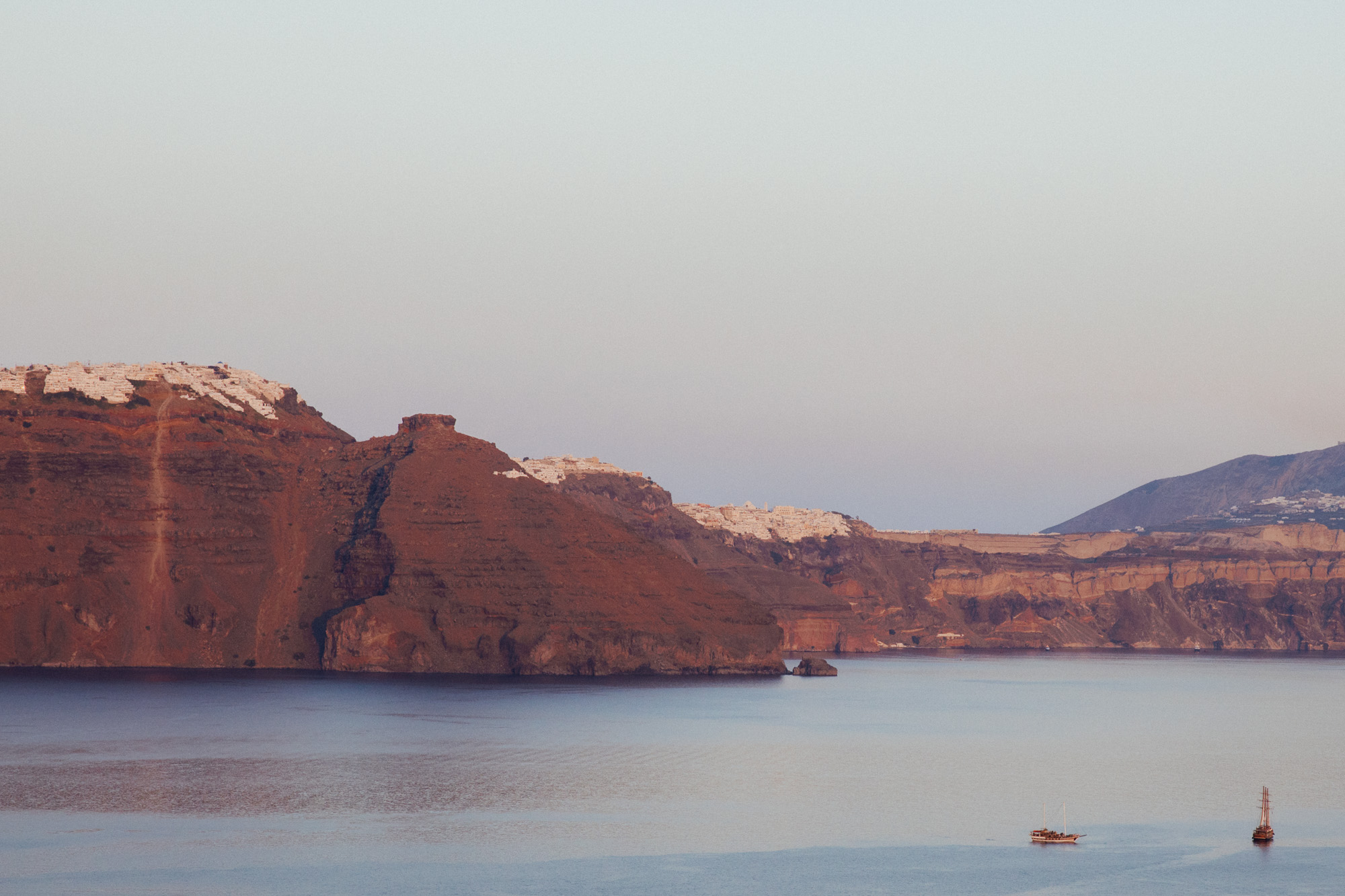 View of Fira Town in Santorini, Greece, as seen from Oia, with its whitewashed buildings and rocky cliffs at sunset.