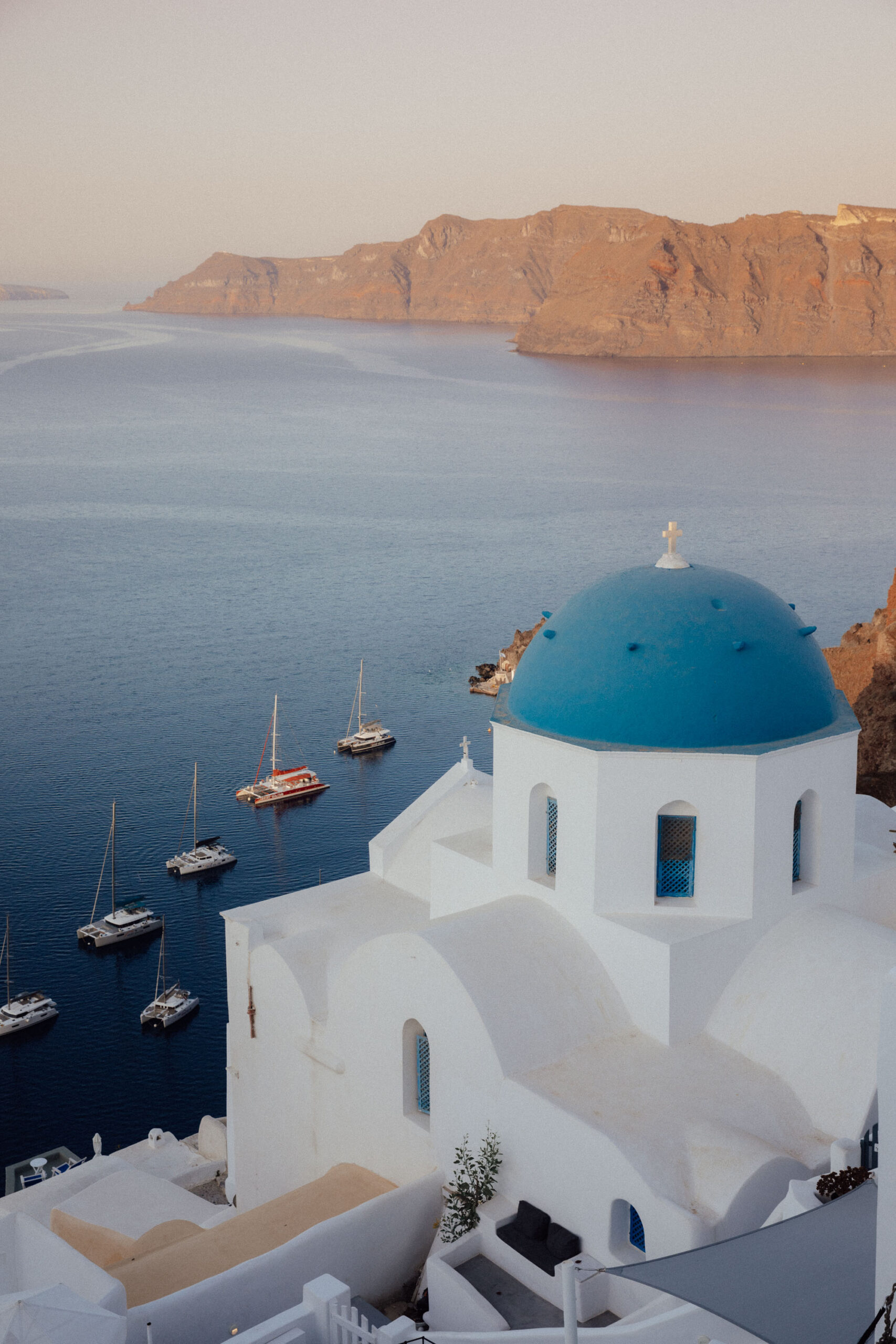 Iconic blue-domed church overlooking the Aegean Sea in Santorini, Greece, during sunset