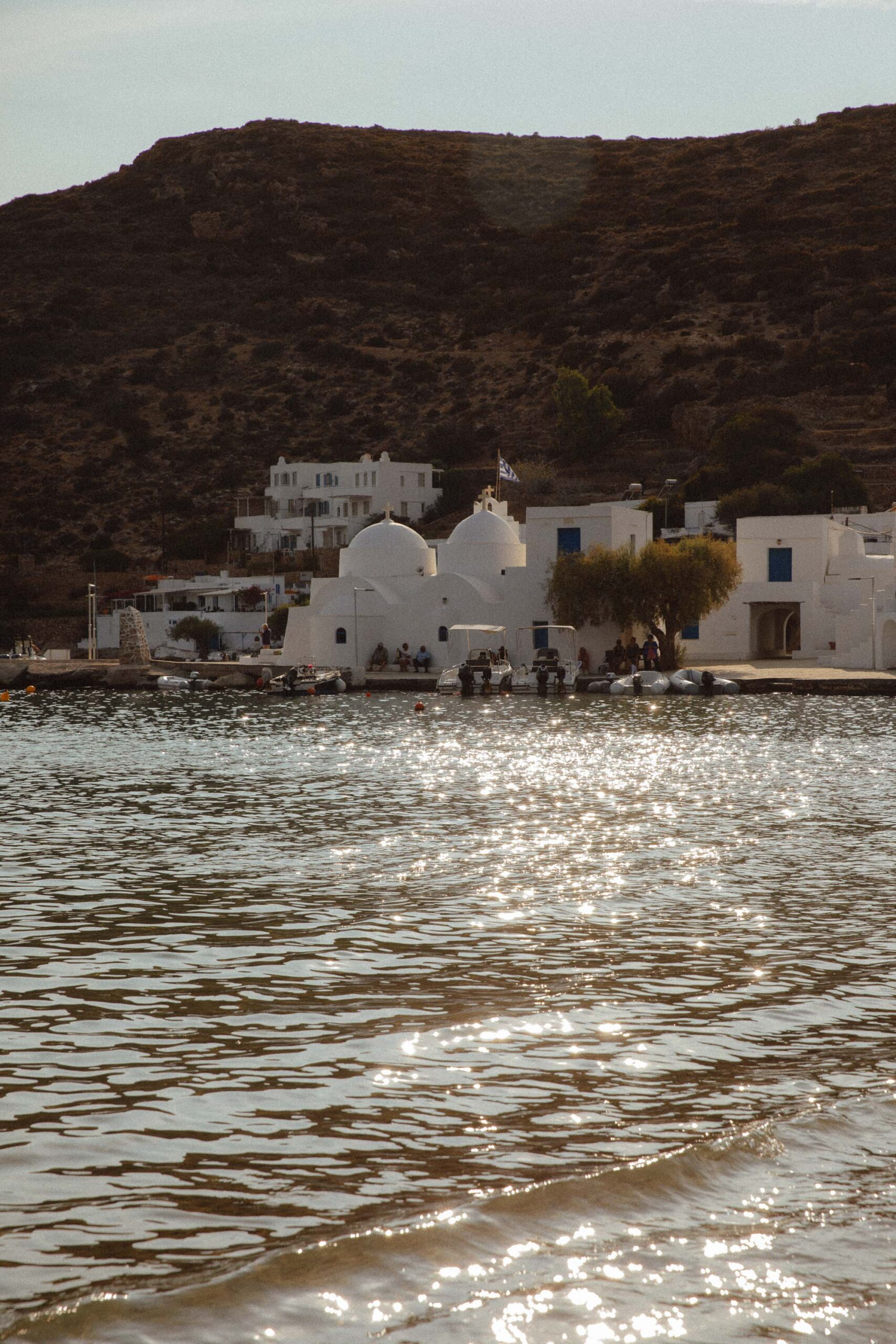 Sunset over Vathy beach in Sifnos with a white church by the water.